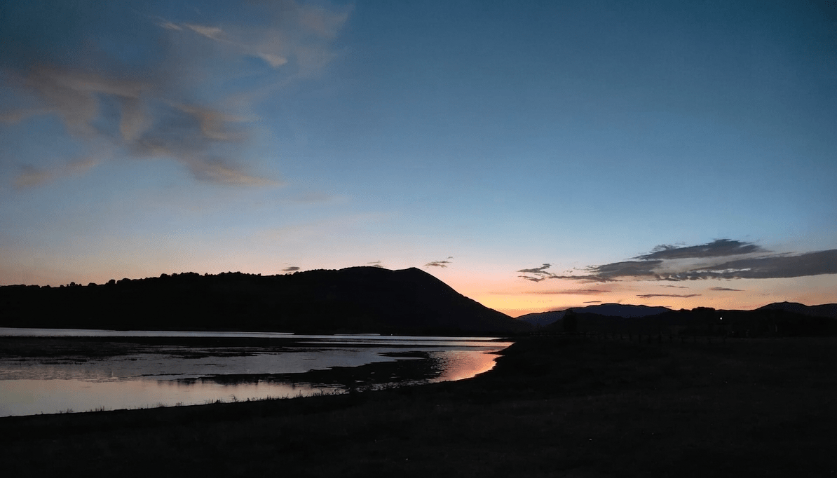 Tramonto sul lago, con le montagne in controluce e una striscia di luce riflessa sull’acqua