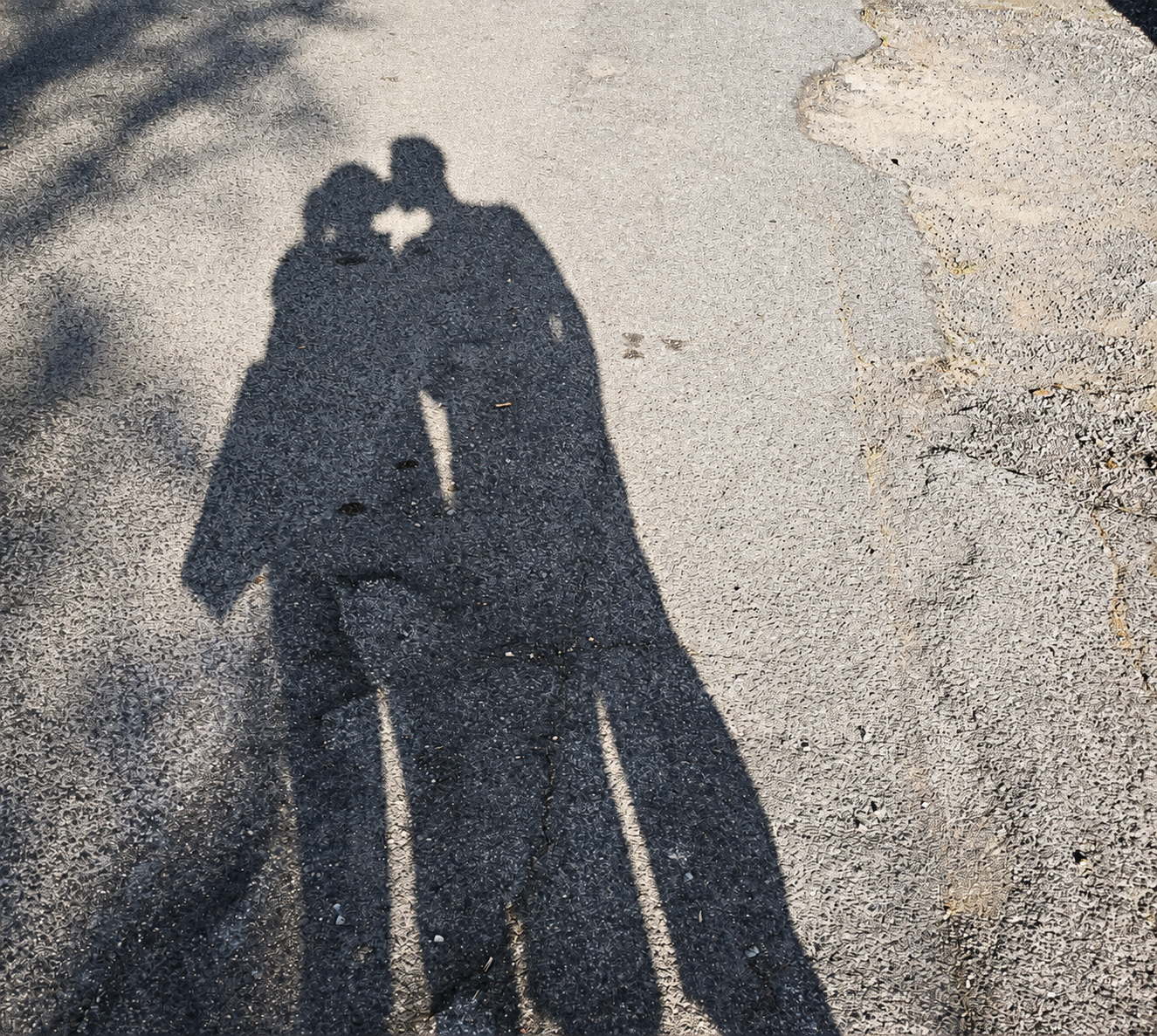 Due ombre vicine sull’asfalto, con uno spazio di luce a forma di cuore fra le teste