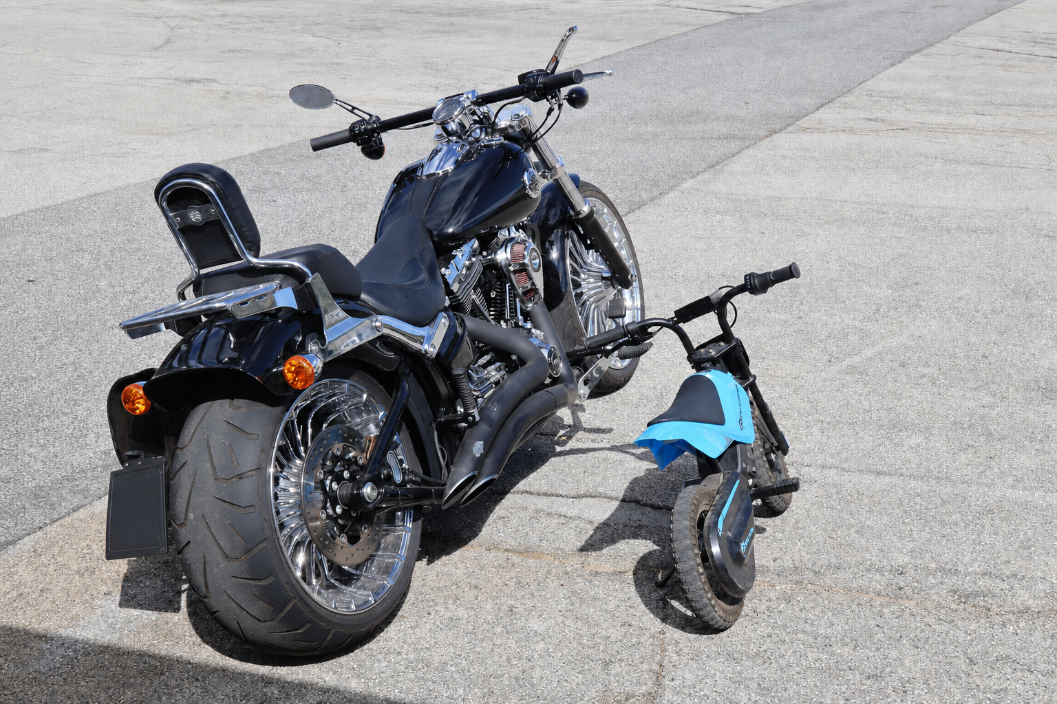 Una grande motocicletta nera e una piccola moto azzurra vicine sull’asfalto