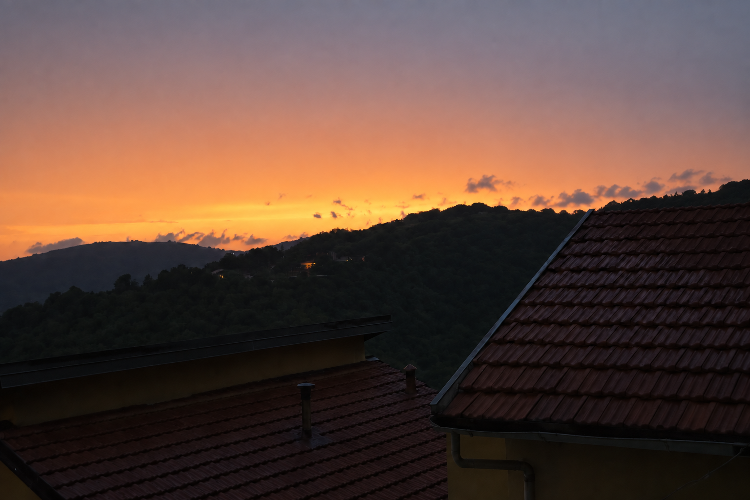La luce calda del tramonto sopra le colline, con i tetti delle case in penombra